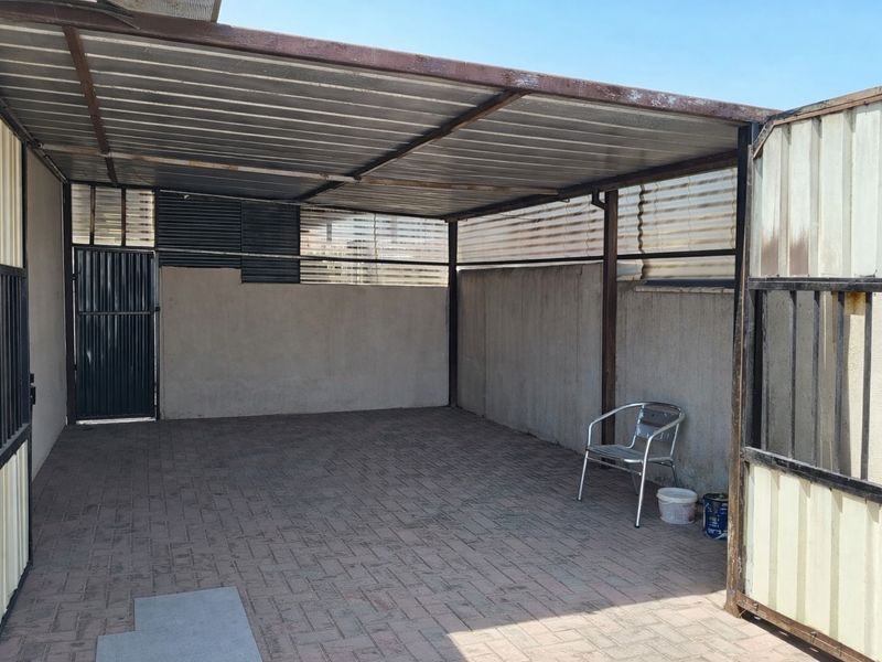 A covered outdoor patio or utility area featuring paved flooring, metal roofing, and perimeter walling with a secure access gate.