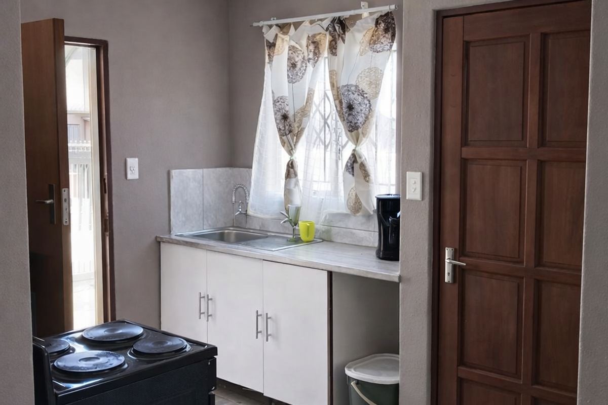 A functional kitchen area featuring white cabinetry, a stainless steel sink, tiled flooring, and a freestanding electric stove.