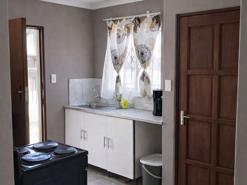 A functional kitchen area featuring white cabinetry, a stainless steel sink, tiled flooring, and a freestanding electric stove.