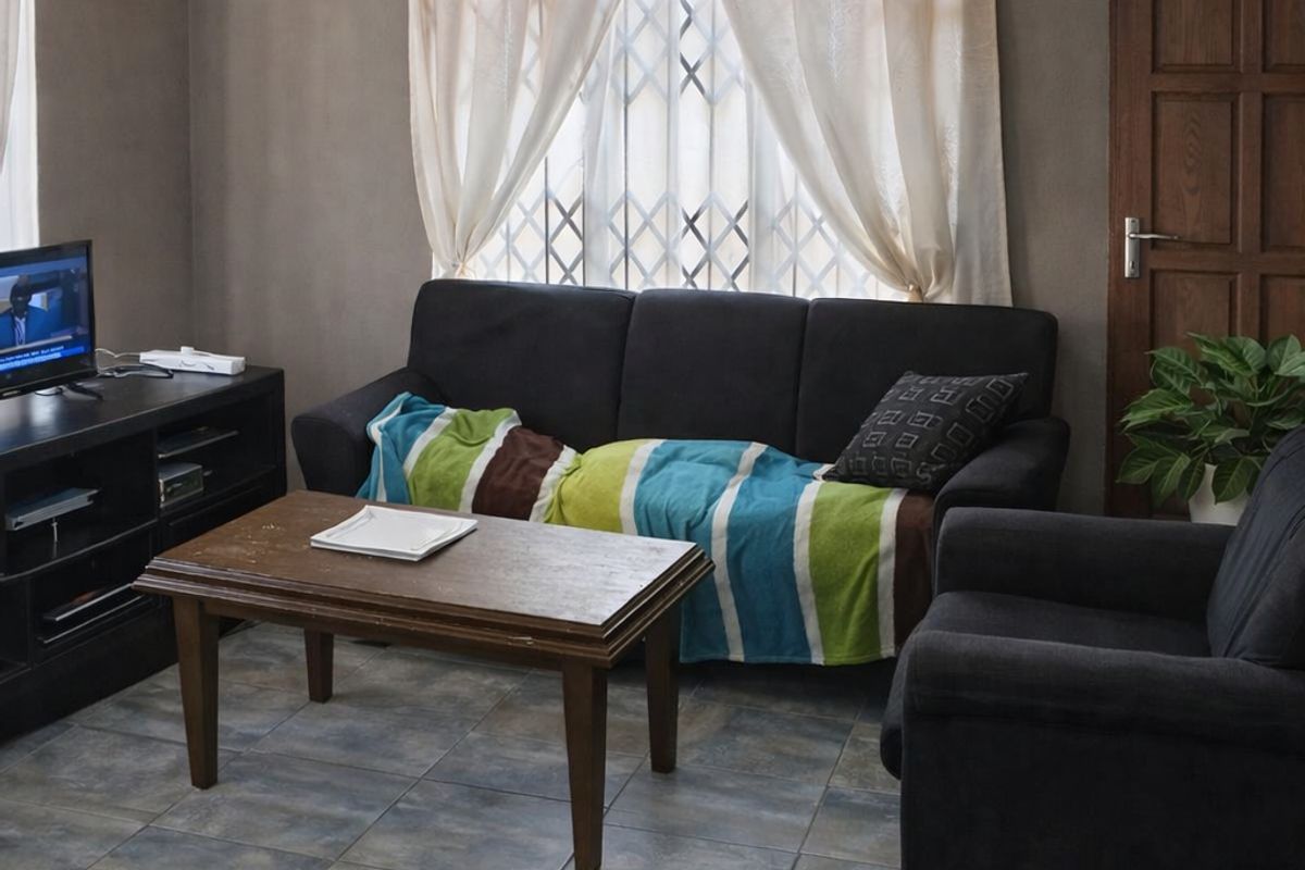 A living room featuring tiled flooring, a window with security gate, and a solid timber door.