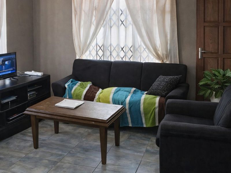 A living room featuring tiled flooring, a window with security gate, and a solid timber door.