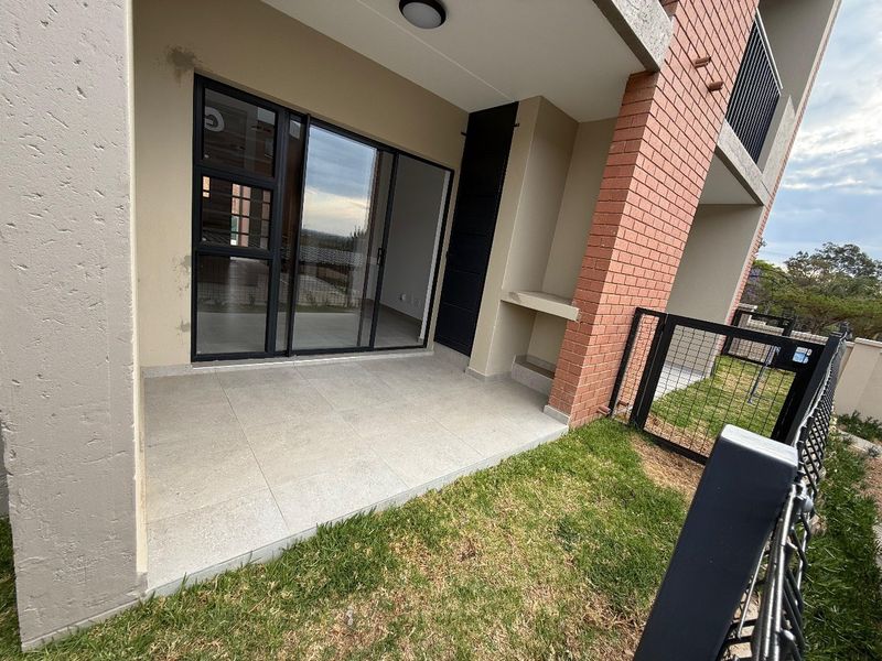 Covered ground floor patio featuring tiled flooring, a built-in braai area, and direct access to a private garden space through sliding glass doors.