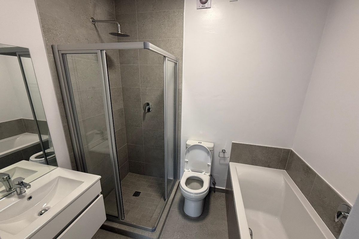 Modern bathroom featuring a glass-enclosed shower, separate bathtub, wall-mounted vanity with basin, and neutral grey tiling.