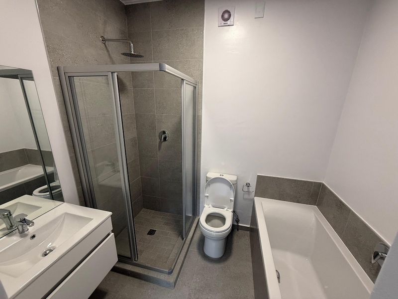 Modern bathroom featuring a glass-enclosed shower, separate bathtub, wall-mounted vanity with basin, and neutral grey tiling.
