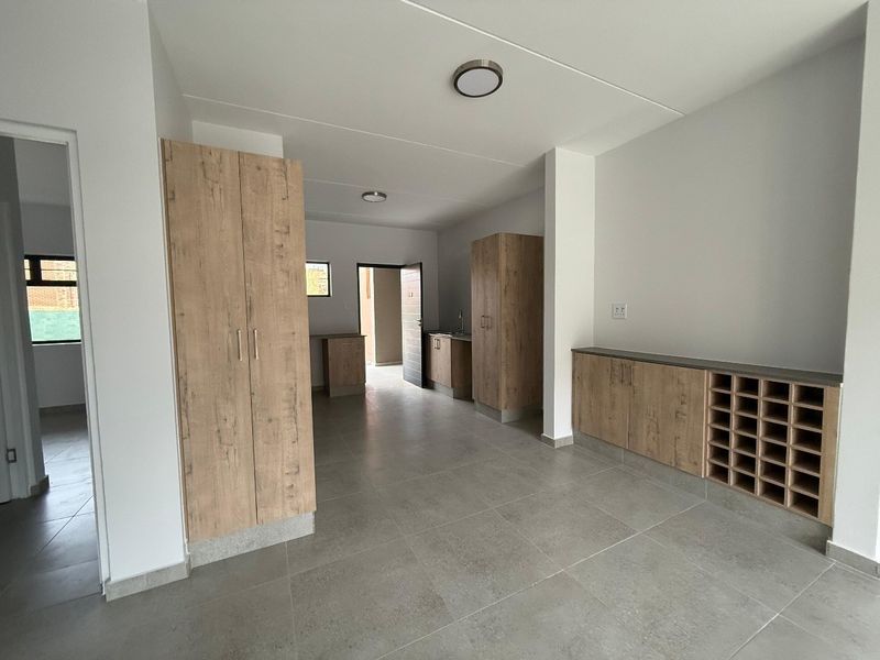 A modern open-plan kitchen area featuring light wood-grain cabinetry, built-in wine storage, and neutral floor tiling throughout the space.
