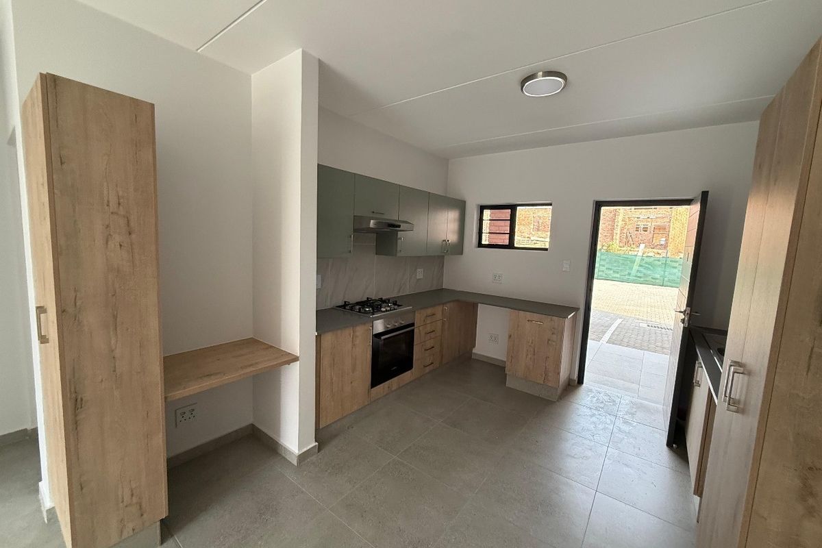 Modern kitchen featuring wood-look cabinetry, built-in oven, gas hob, extractor fan, and tiled flooring with direct access to the exterior.