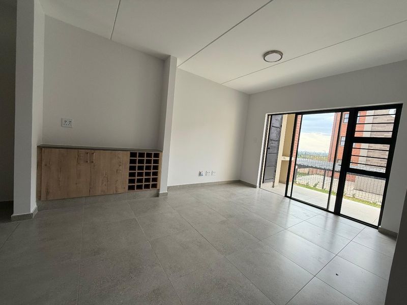 A bright, open-plan living area featuring modern floor tiles, a built-in wooden storage unit, and large sliding glass doors leading to an outdoor space.