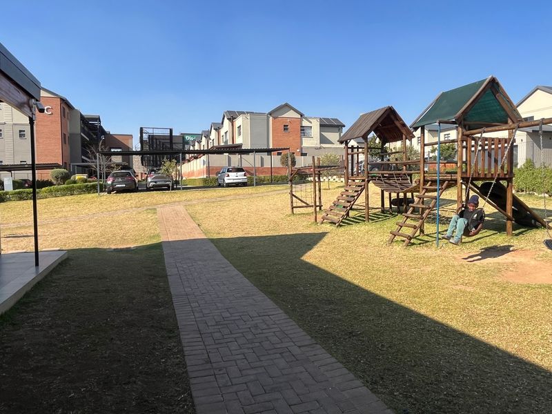 Communal garden area featuring a paved walkway and children's playground equipment within a residential apartment complex.