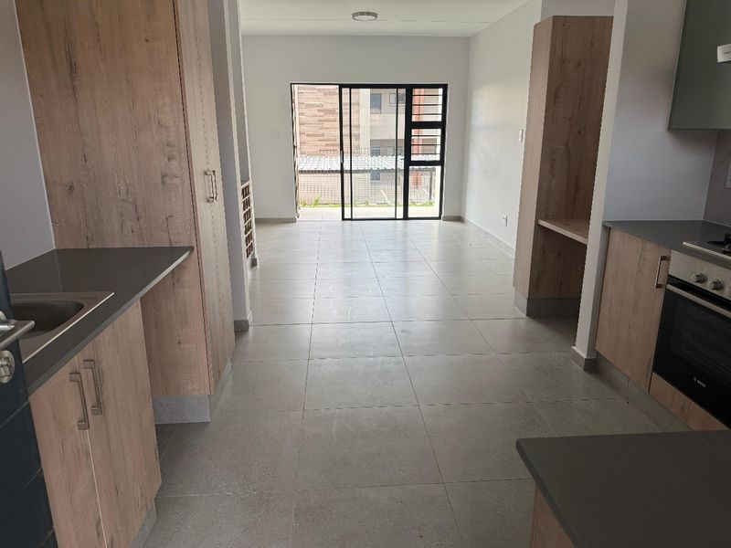 Open-plan kitchen and living area featuring modern wood-finish cabinetry, built-in oven, hob, and tiled flooring leading to a sliding door entrance.