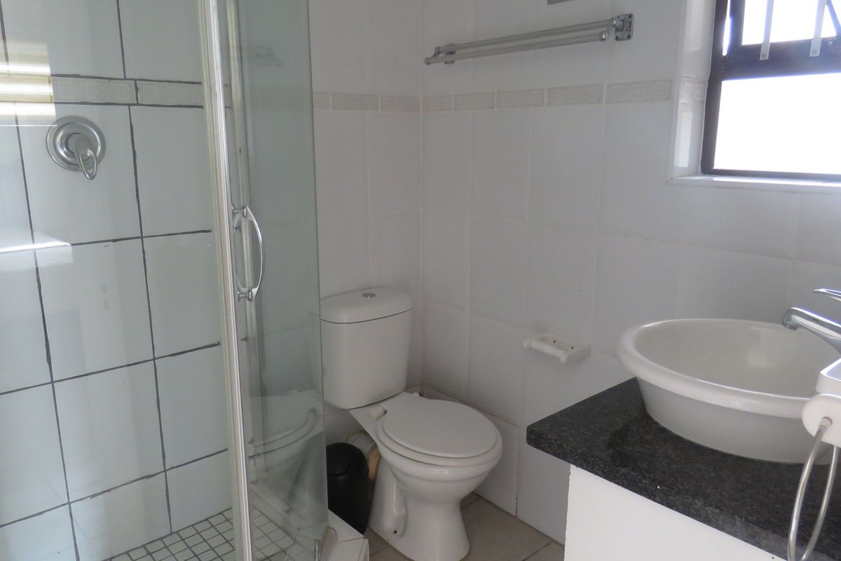 A functional bathroom featuring a glass-enclosed shower, a white toilet, and a vanity with a countertop basin.