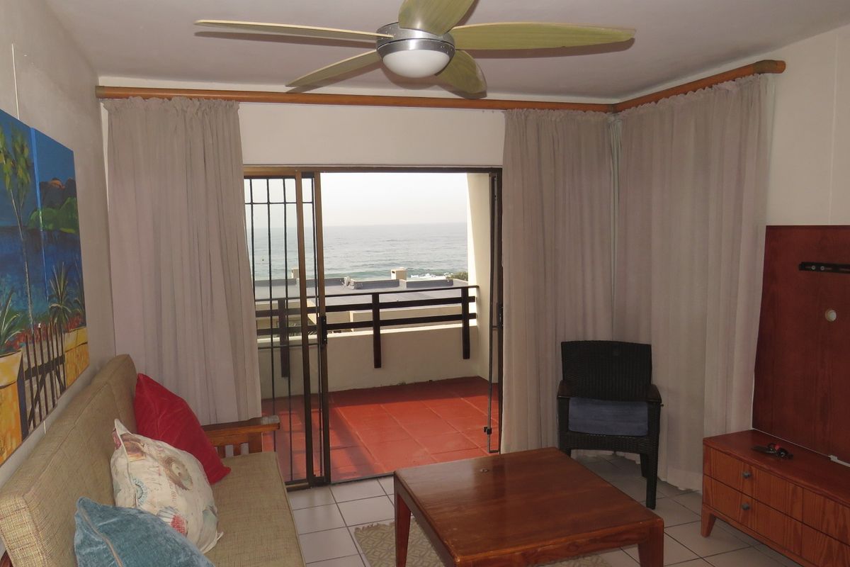 Living room featuring tiled flooring, a ceiling fan, and sliding glass doors opening onto a balcony with ocean views.