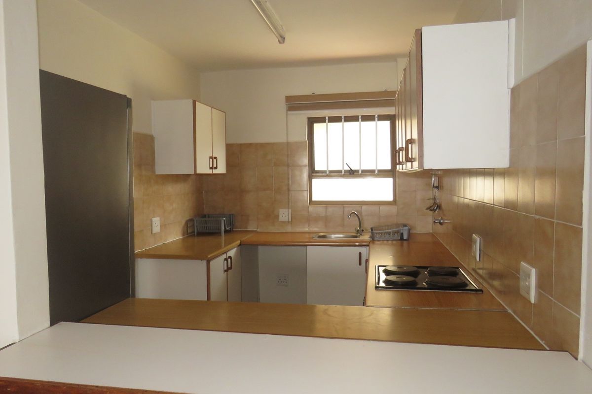 A functional kitchen featuring built-in cabinetry, a tiled backsplash, a built-in electric hob, and a stainless steel sink under a window.