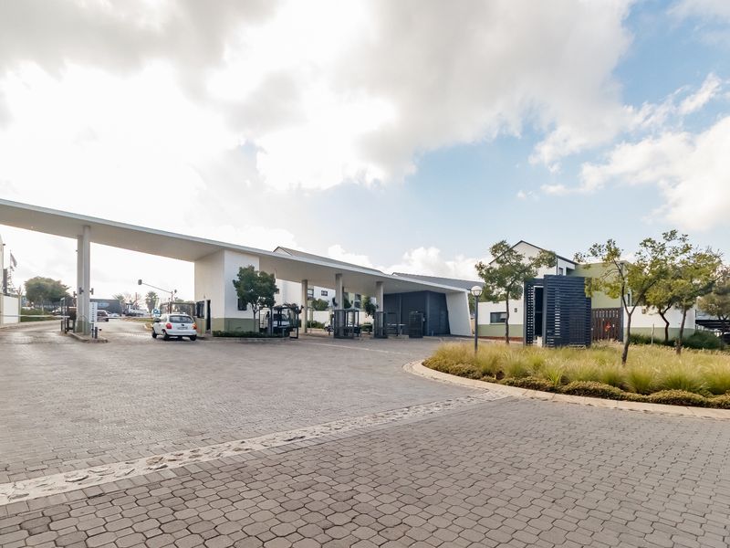 The main entrance and security gatehouse of the apartment complex, featuring a paved driveway and modern architectural design.