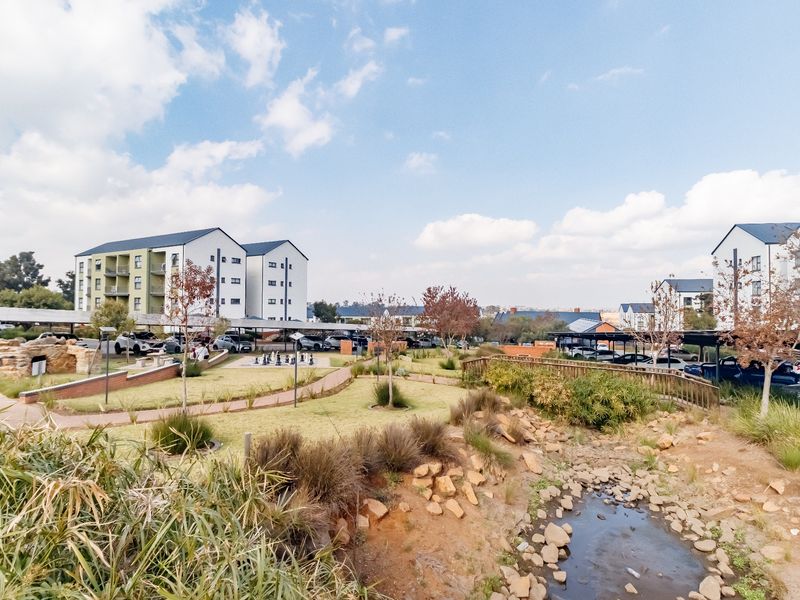 A well-maintained residential complex featuring landscaped gardens, paved walkways, a stone water feature, and convenient covered parking facilities.