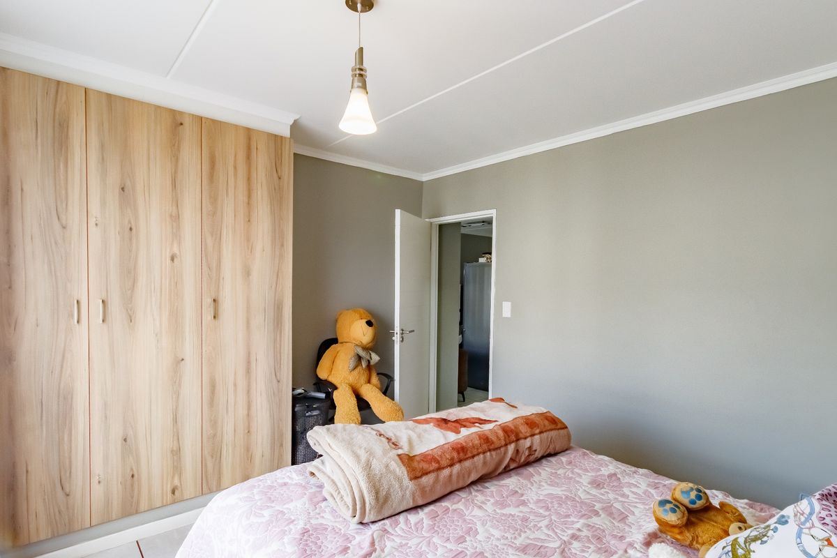A well-maintained bedroom featuring light wood-grain built-in cupboards, neutral wall tones, and a modern pendant light fixture.