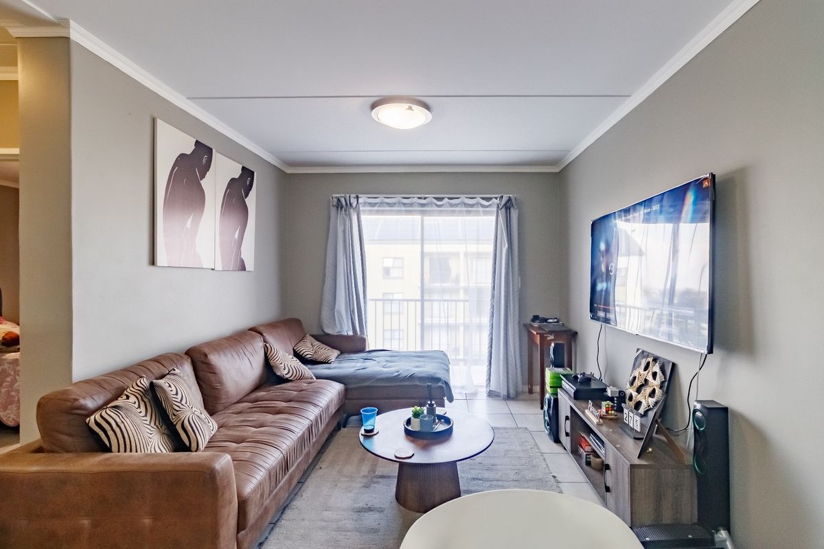 A well-maintained living room featuring tiled flooring, neutral wall tones, and a sliding glass door providing access to a balcony.