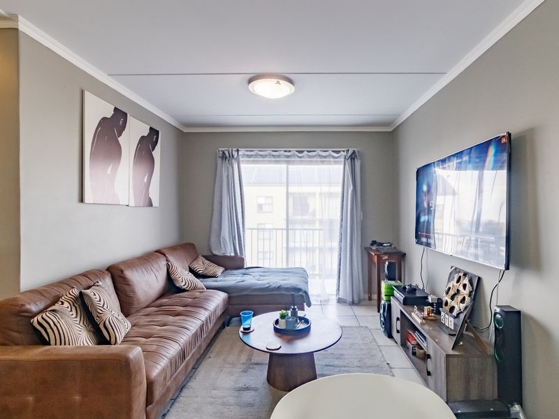 A well-maintained living room featuring tiled flooring, neutral wall tones, and a sliding glass door providing access to a balcony.