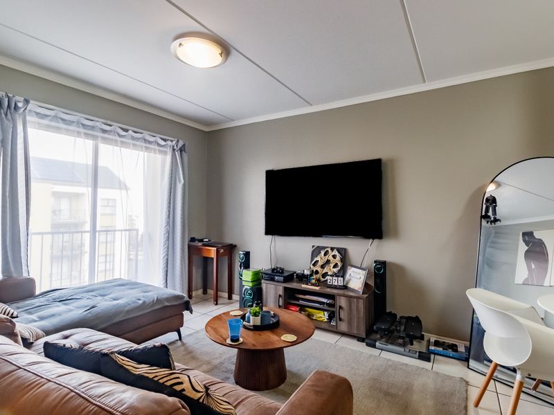 A comfortable living room featuring tiled flooring, a ceiling light fixture, and a sliding glass door providing access to an outdoor balcony area.