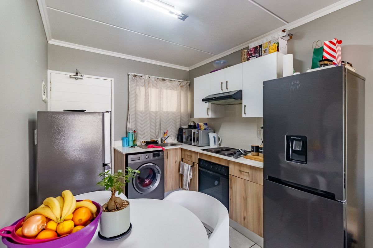 Compact kitchen featuring light wood-finish cabinetry, white upper cupboards, built-in oven and hob, and an integrated washing machine.