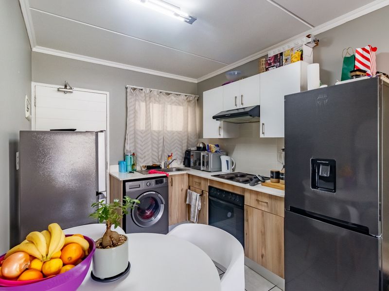 Compact kitchen featuring light wood-finish cabinetry, white upper cupboards, built-in oven and hob, and an integrated washing machine.