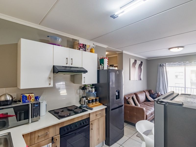 Open-plan kitchen and living area featuring modern cabinetry, built-in cooking appliances, tiled flooring, and access to a balcony through sliding glass doors.