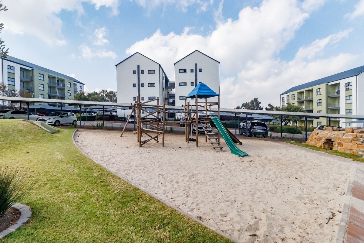 Communal outdoor area featuring a sand-based playground, landscaped lawn, and covered parking bays within the apartment complex grounds.