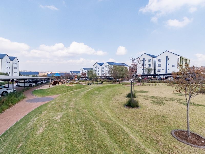 A view of the apartment complex grounds featuring landscaped lawns, paved walkways, and covered parking facilities within a well-maintained residential estate.