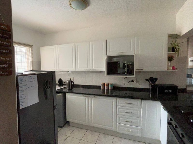 A functional kitchen featuring white cabinetry, dark granite countertops, tiled flooring, and built-in oven and microwave appliances.