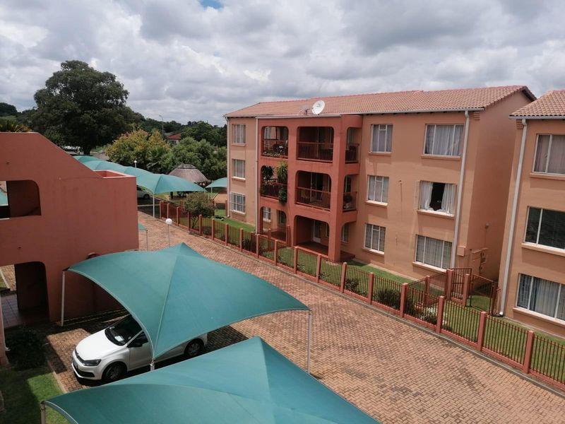 Elevated view of an apartment complex featuring paved parking areas with shade cloth carports and multi-story residential units with private balconies.