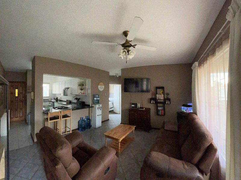 Open plan living area featuring tiled flooring, a ceiling fan, and a pass-through kitchen with built-in cabinetry and countertops.