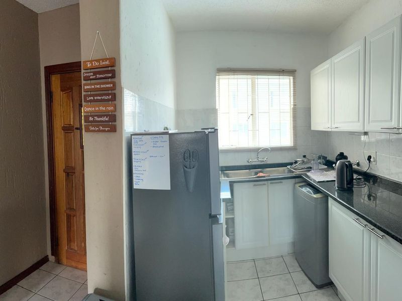 A functional kitchen featuring white cabinetry, dark granite countertops, a stainless steel sink, and tiled flooring with a window for natural light.