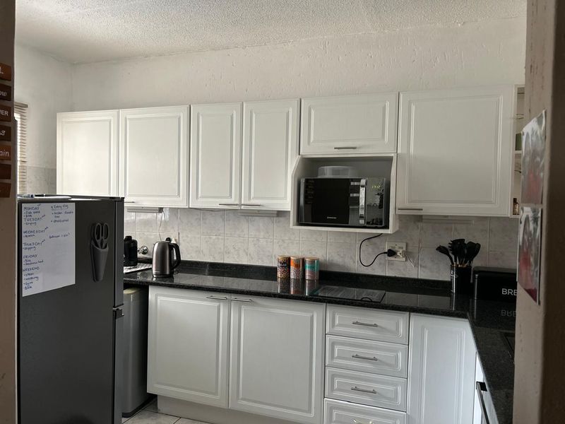 A functional kitchen featuring white cabinetry, dark granite countertops, a tiled backsplash, and a built-in microwave housing unit.