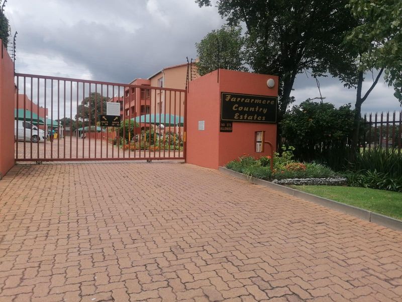 The secure gated entrance to Farrarmere Country Estates, featuring a paved driveway, perimeter fencing, and clear signage for the apartment complex.