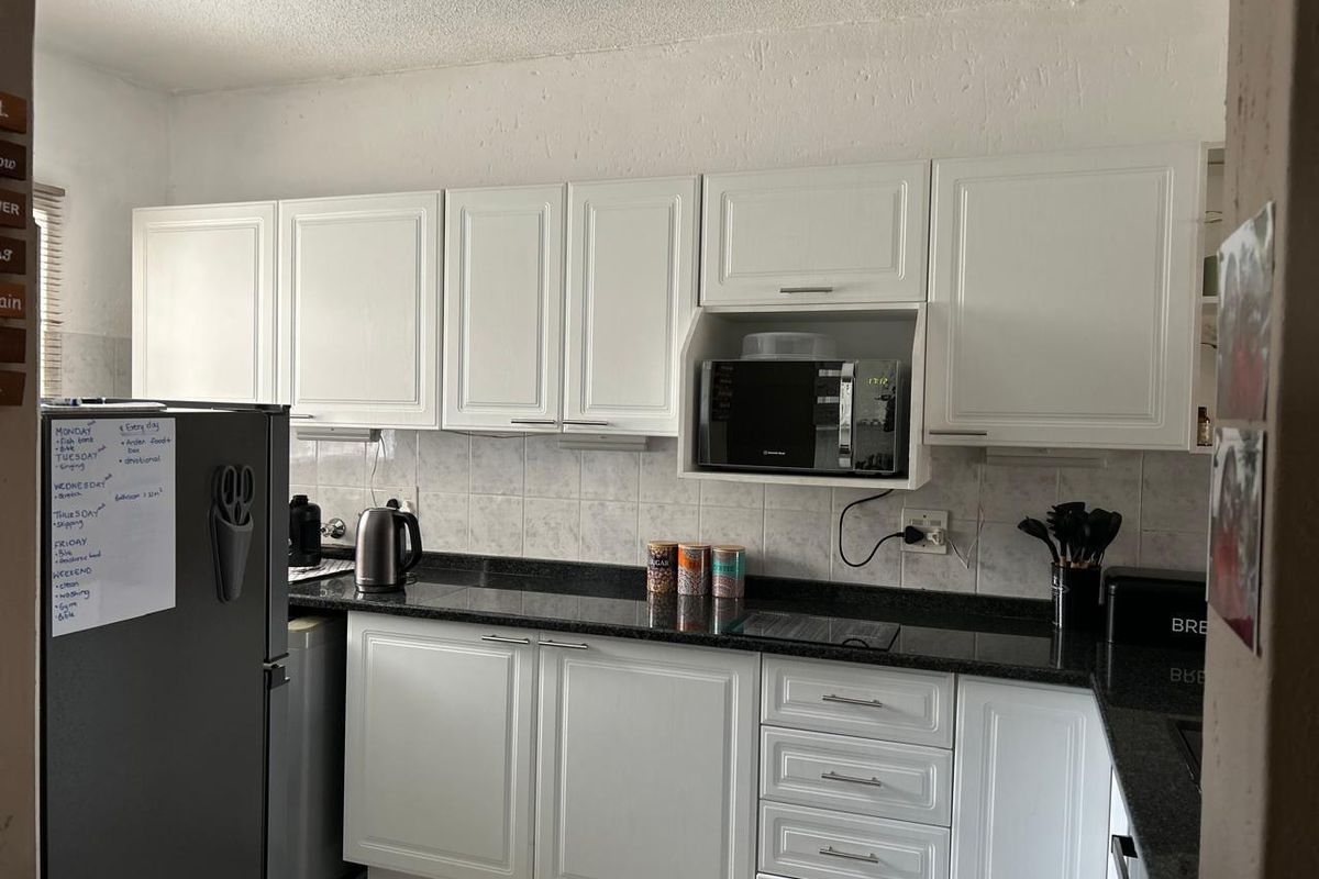A functional kitchen featuring white cabinetry, dark granite countertops, a tiled backsplash, and a built-in microwave housing unit.