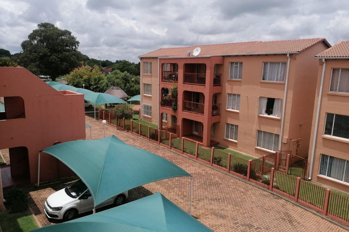 Elevated view of an apartment complex featuring paved parking areas with shade cloth carports and multi-story residential units with private balconies.