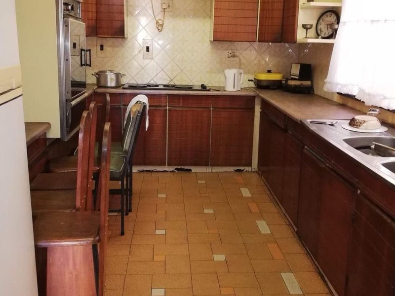 A dated kitchen featuring wood-finish cabinetry, built-in oven, extractor fan, and tiled flooring, offering a functional layout with potential for modernization.