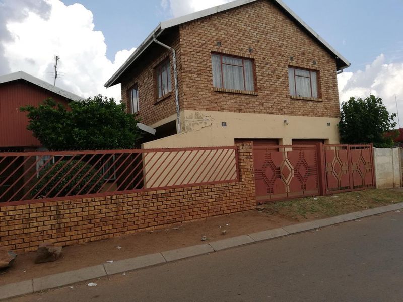 Two-story brick residential property featuring a double garage, perimeter wall with metal fencing, and a tiled roof.
