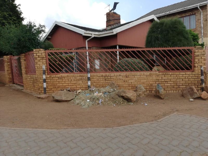 Street view of a residential property featuring a brick boundary wall, metal fencing, and a tiled roof structure.
