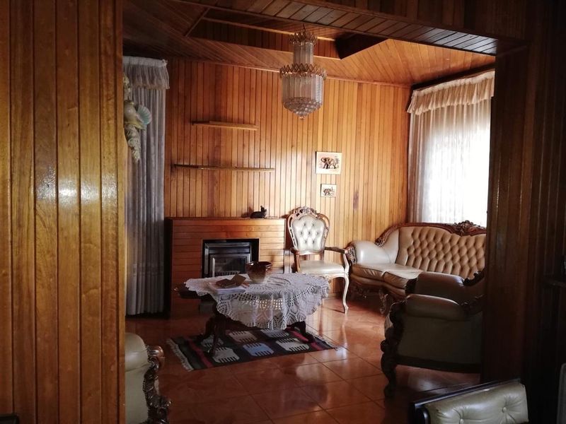 A living room featuring extensive wood-paneled walls and ceiling, a built-in fireplace, and tiled flooring, offering a traditional and cozy atmosphere.
