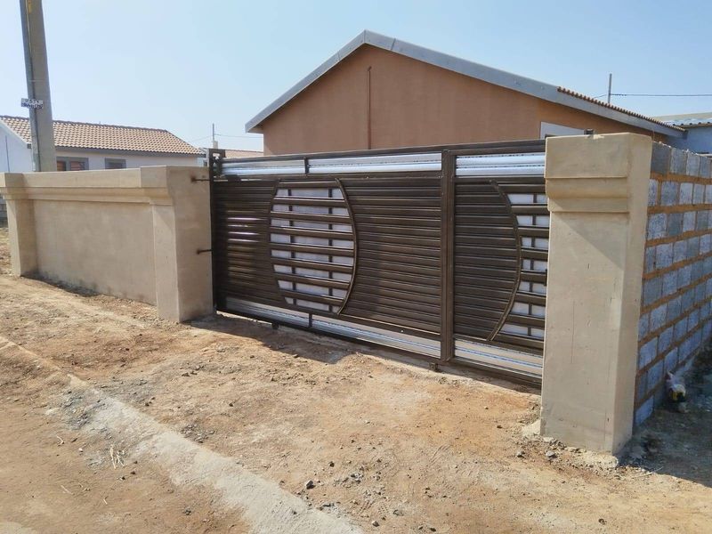 A secure metal sliding gate installed within a partially finished boundary wall, providing access to the property frontage.