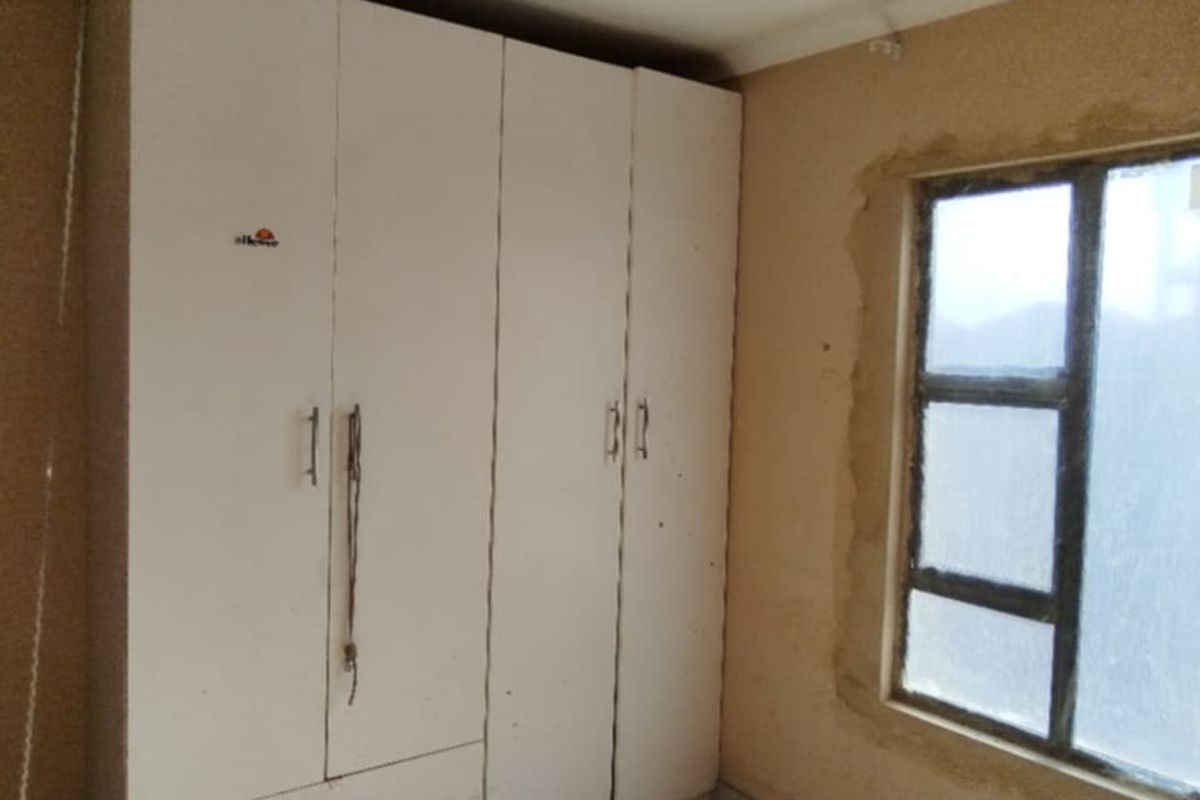 Bedroom featuring a built-in wardrobe and a window with unfinished plasterwork around the frame, requiring cosmetic repairs and painting.