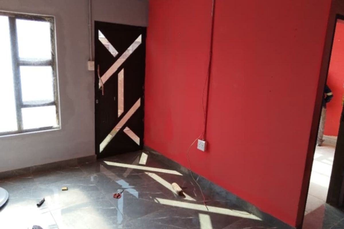An interior room featuring tiled flooring, a decorative security door, and exposed electrical wiring on a red accent wall.