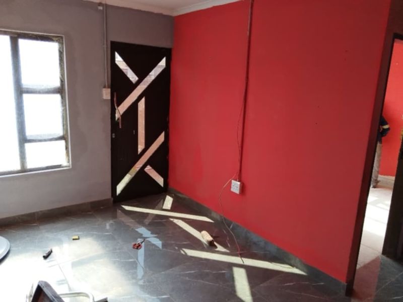 An interior room featuring tiled flooring, a decorative security door, and exposed electrical wiring on a red accent wall.
