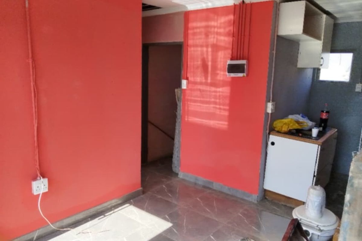 A small utility or kitchen area featuring tiled flooring, exposed electrical conduits, and basic cabinetry, currently in need of renovation and finishing.
