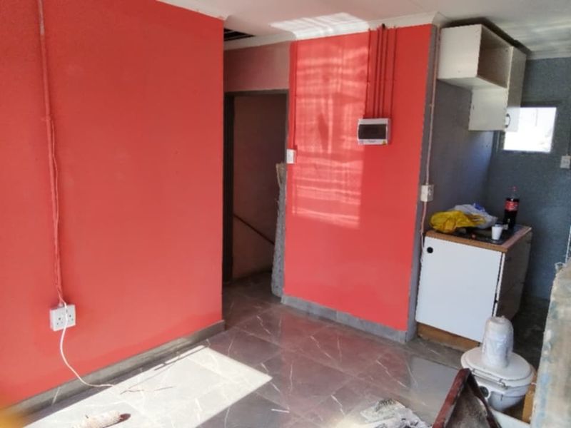A small utility or kitchen area featuring tiled flooring, exposed electrical conduits, and basic cabinetry, currently in need of renovation and finishing.