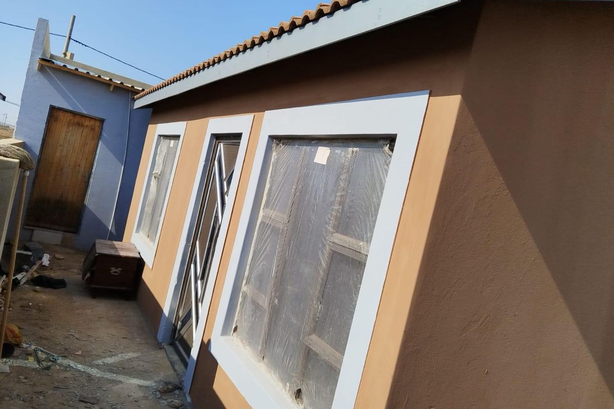 Exterior view of a residential building featuring brown rendered walls, tiled roof, and window frames with protective plastic film still attached.