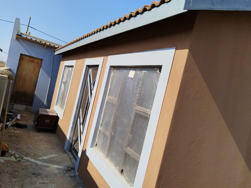Exterior view of a residential building featuring brown rendered walls, tiled roof, and window frames with protective plastic film still attached.