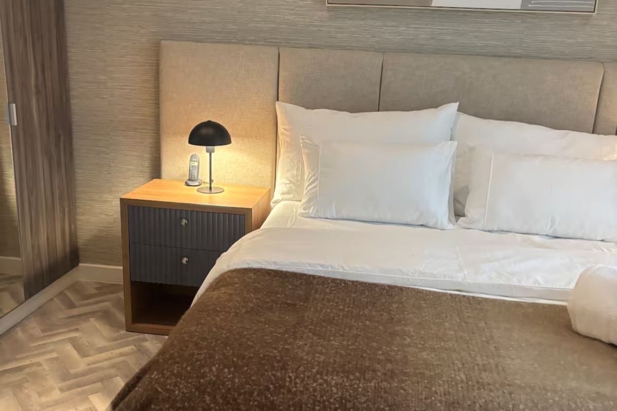 A well-appointed bedroom featuring modern herringbone flooring, a neutral upholstered headboard, and integrated built-in wardrobe storage.