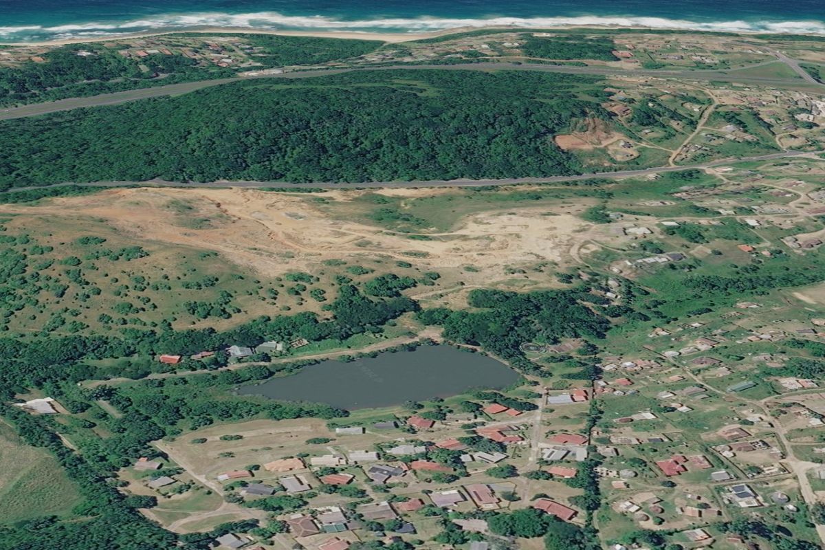 An aerial view of a coastal residential area featuring a natural lake, surrounding greenery, and proximity to the ocean.
