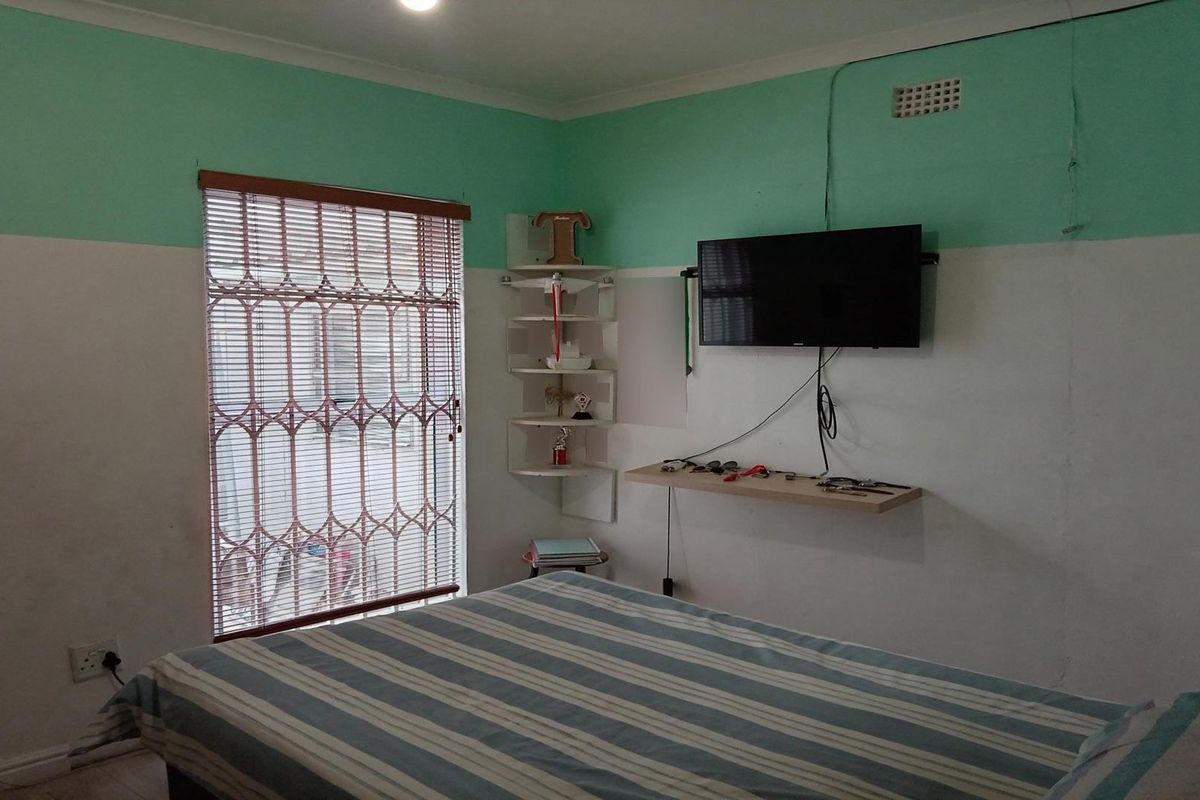 A bedroom featuring a security gate on the window, built-in corner shelving, and a wall-mounted television shelf.